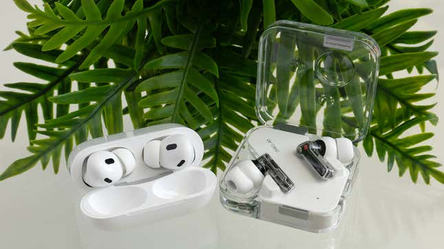 The Nothing Ear (2) wireless earbuds sitting in their open charging case next to the Apple AirPods Pro 2 inside their open charging case, in front of a green plant.