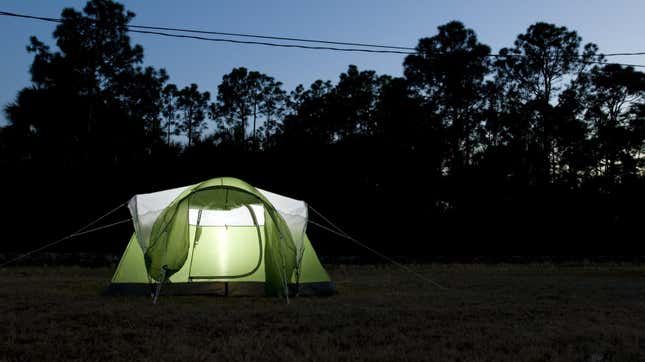 An illuminated green pop-up tent in a dark backyard with trees and power lines visible in the background