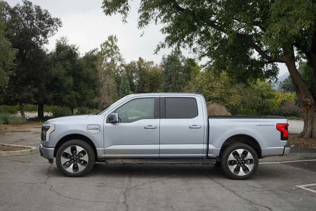 A silver 2023 Ford F-150 Lightning is parked in profile near some trees