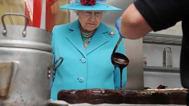Queen Elizabeth watches as a person pours chocolate sauce out of a ladle