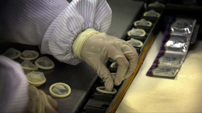 A condom assembly line with a worker's gloved hand.