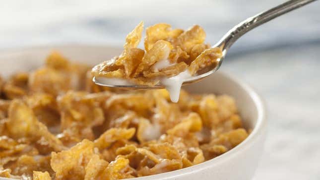 Cereal bowl of cornflakes and milk with spoon lifting a bite from the bowl