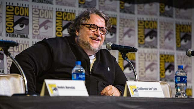 Guillermo del Toro sits at a San Diego Comic-Con dais and speaks into a microphone. 