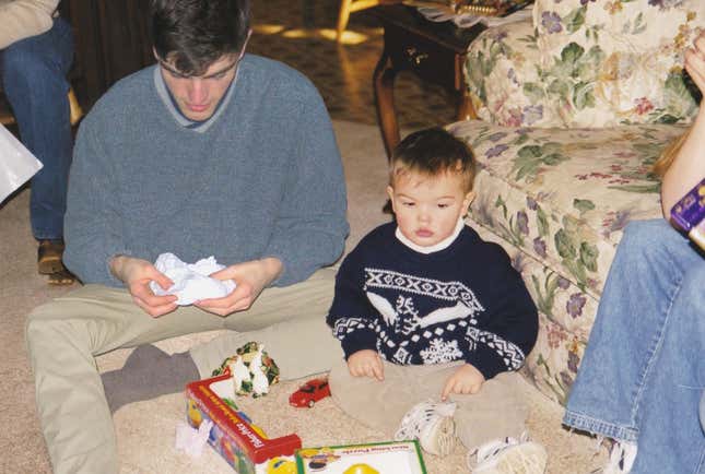 Adult Nickerson handles gift paper while young Nickerson looks at his Christmas toys.