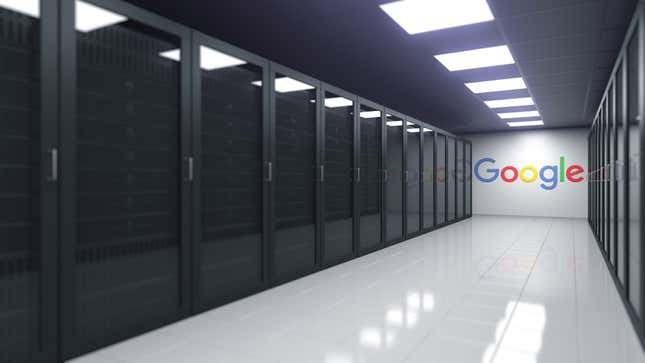 A bank of computer server banks behind glass panes leading down a hall toward the Google logo.