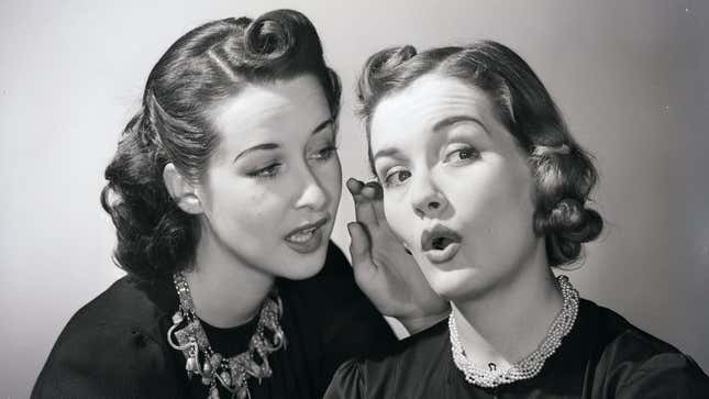 A vintage black and white portrait-style photo of a woman whispering into the ear of another woman, who looks surprised