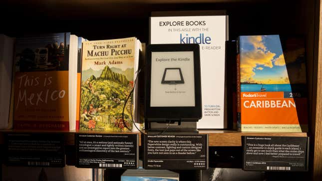 A Kindle device next to a series of physical books.