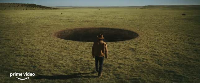 A man dressed in cowboy attire strides toward a giant hole in the ground.