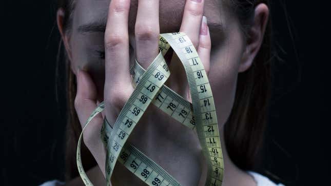 An image of a woman holding a tape measure to her face.