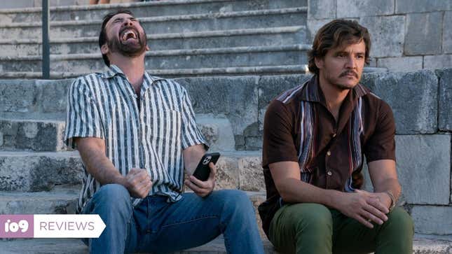 Nic Cage laughing with a mobile phone in his hand, as Pedro Pascal glumly stares while sitting next to him.