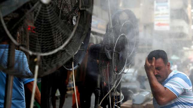 A man stands by fans spraying air mixed with water vapor deployed by donors to cool down pedestrians along a street in Iraq's capital Baghdad on June 30, 2021 amidst a severe heat wave.