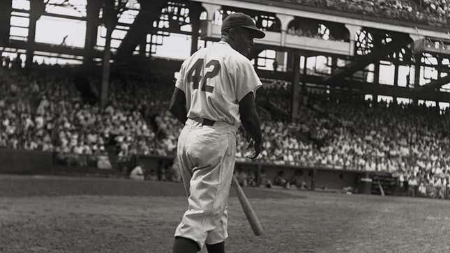 American baseball player Jackie Robinson, second baseman for the Brooklyn Dodgers, steps up to bat with his back to the camera during a game at a packed stadium.