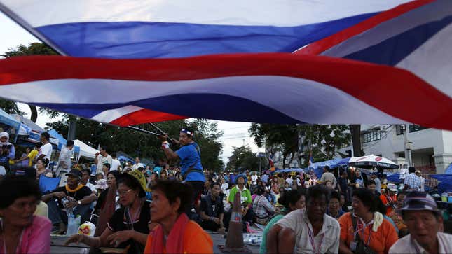 An anti-government protester waves national flags over other protesters gathering in the street near their main encampment after a coup in central Bangkok.