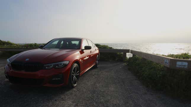 A photo of the front end of an orange BMW 330e sedan in a parking lot near the sea.