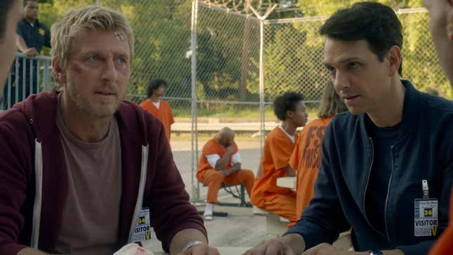 William Zabka's Johnny Lawrence and Ralph Macchio's Daniel LaRusso are wearing visitor badges while sitting in the yard of a prison in Cobra Kai.