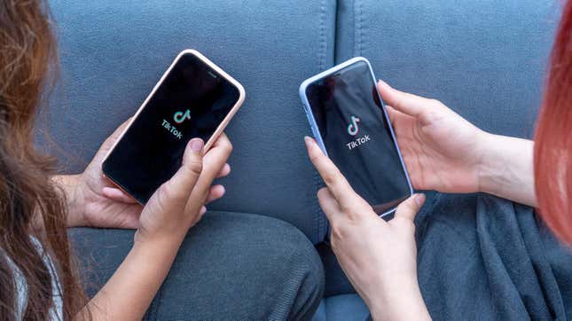 Two teenage girls look at smartphones displaying the TikTok app logo