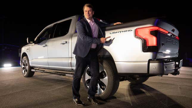 Ford CEO Jim Farley poses with an F-150 Lighting, gesturing to its logo near the tailgate.