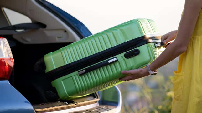 woman packing suitcase into truck of car