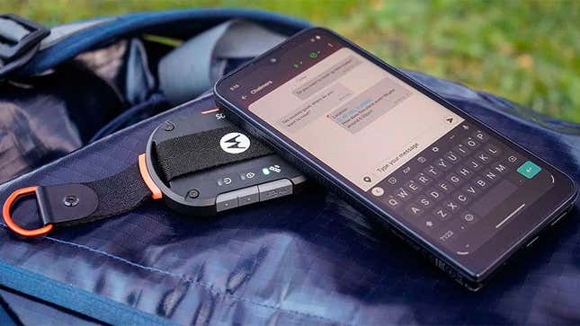 The Motorola Defy under a smartphone using a satellite messaging app, while both are sitting on a backpack.
