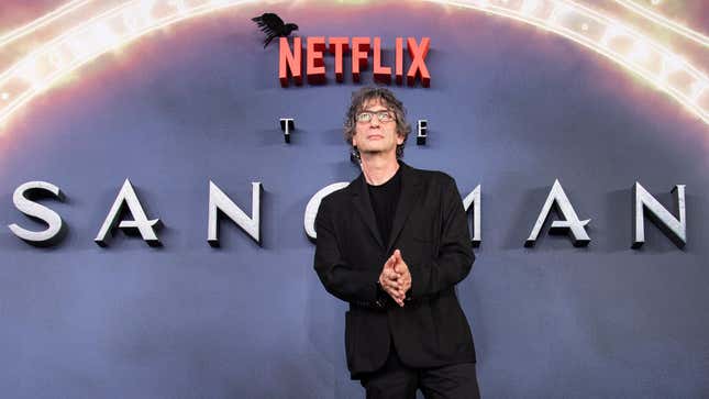 Neil Gaiman in front of the Sandman logo.