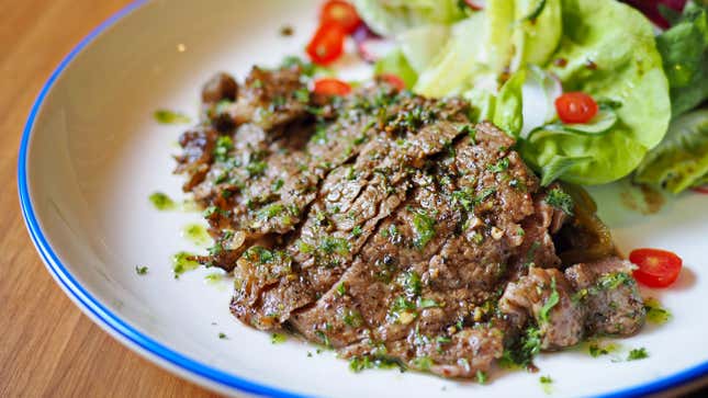 A cut of grilled beef plated next to a salad