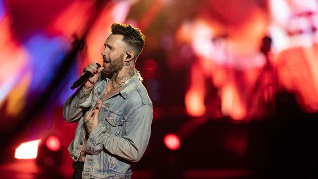 A photo of Adam Levine singing on stage. 