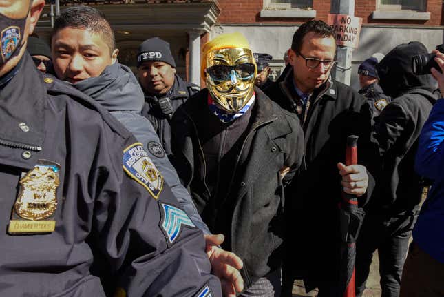 A man in a gold Anonymous mask is detained at a protest against Drag Queen story hour outside of The Center, a support space for LGBTQ+ people on March 19, 2023 in New York City. 