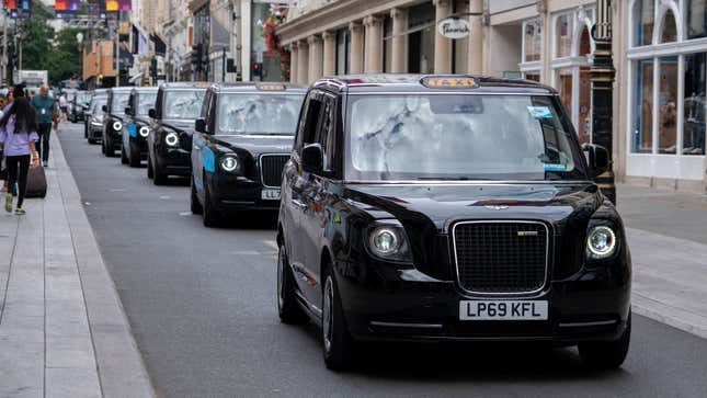 A photo of a line of black London taxis driving on a street. 