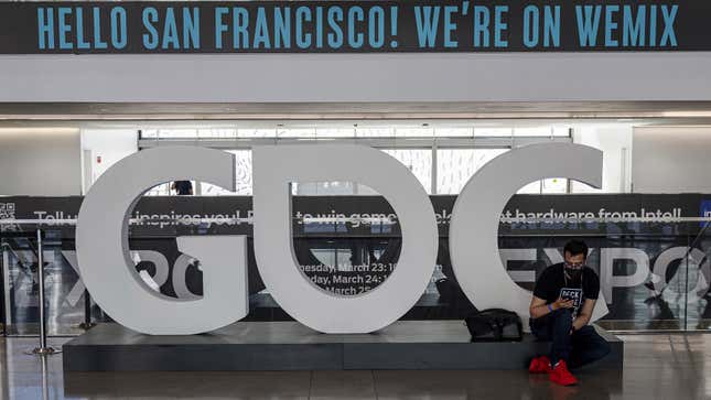 A GDC 2022 attendee sits on the base of a large sculpture of the letters 'GDC'