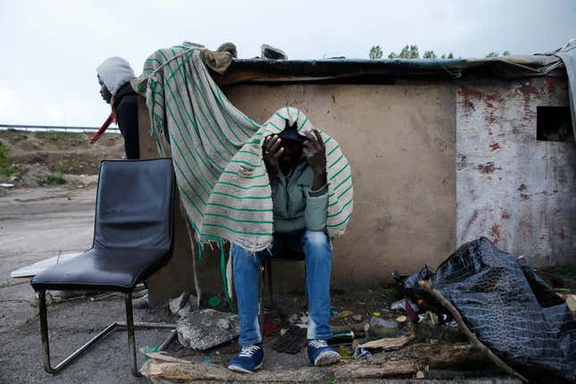 Two migrants from the Sudan protect themselves from the rain as they wait near a road where lorries pass in Calais.