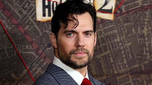 Henry Cavill stares at the camera while wearing a grey striped suit. 
