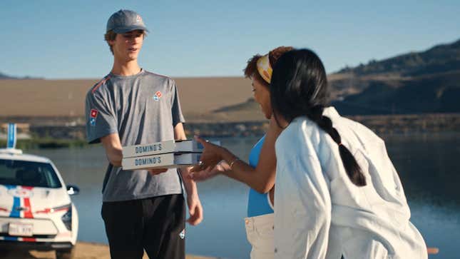 Un repartidor de Domino's entregando dos pizzas a dos personas al lado de un lago.