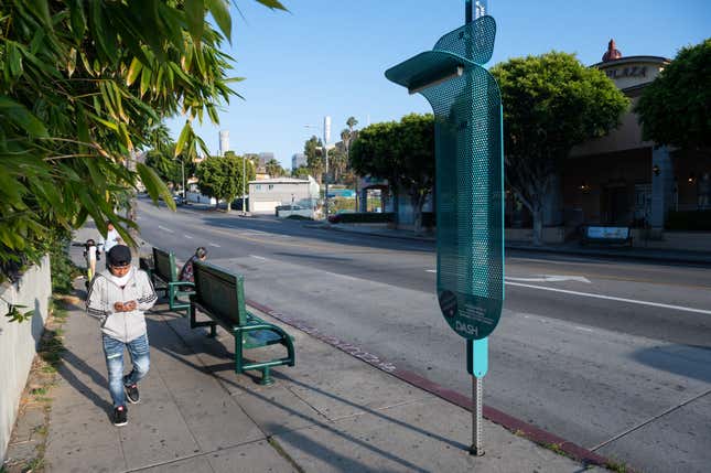 A light blue perforated metal bus shelter prototype is installed on a Los Angeles bus stop sign.