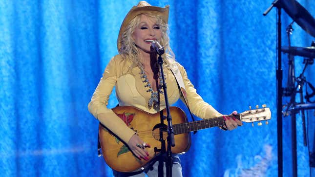 A photo of Dolly Parton on stage in a yellow outfit playing the guitar. 