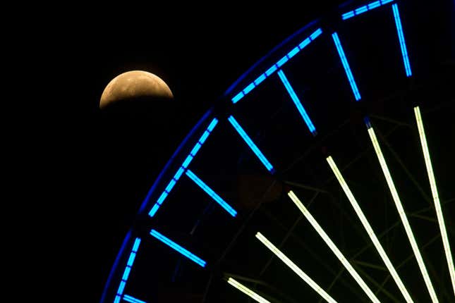 The lunar eclipse progresses is seen behind a ferris wheel over Santa Monica Beach in Santa Monica, Calif., Wednesday, May 26, 2021.