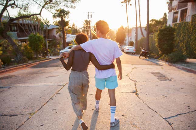 frican American couple with their arms around each other walking down a suburban street at sunset shot from behind