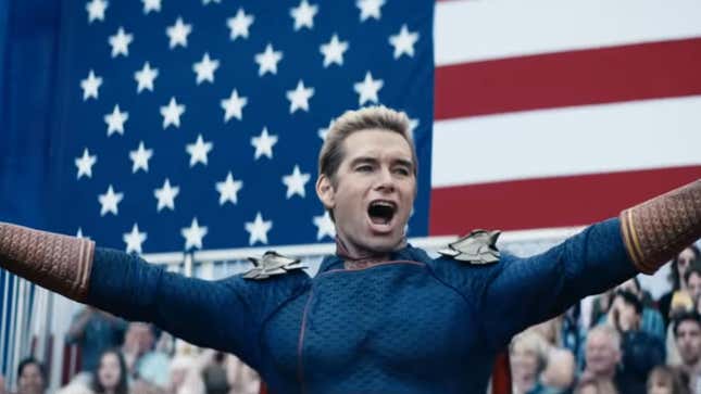 Antony Starr's Homelander stands before a cheering crowd and a giant American flag in his superhero costume with his arms raised.