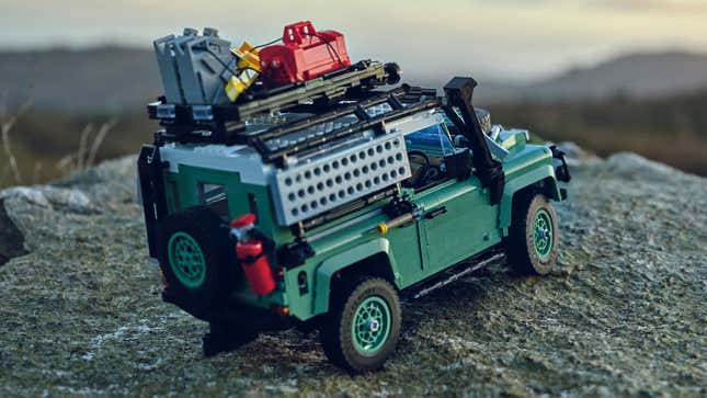 The Lego Land Rover Defender 90 model parked on a rock in an outdoors setting.