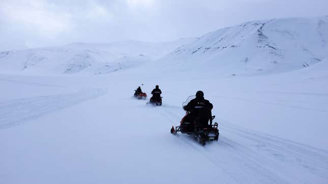 Three people riding snowmobiles in the mountains. 