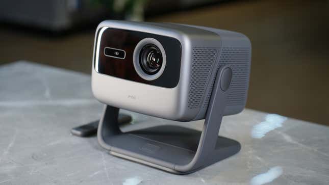 The JMGO N1 Ultra 4K projector sitting on a marble table with a small wireless remote next to it.
