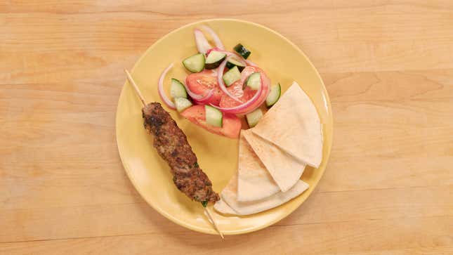 Plate with meat skewer, salad, and pita triangles
