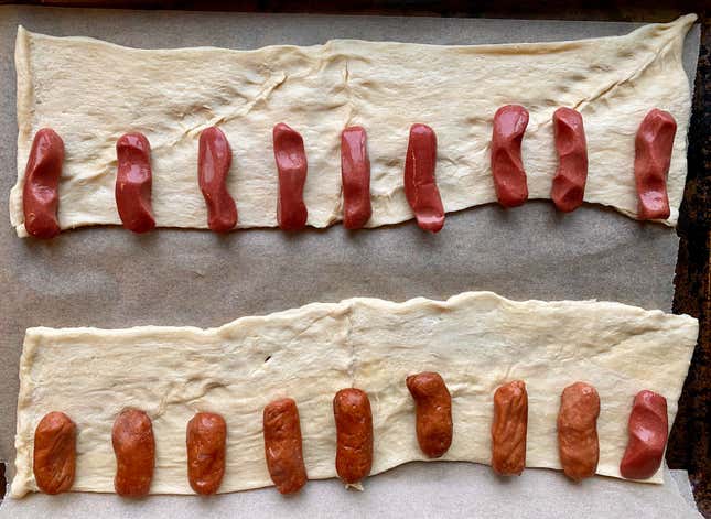 Mini hot dogs lined up on a strip of crescent roll dough.