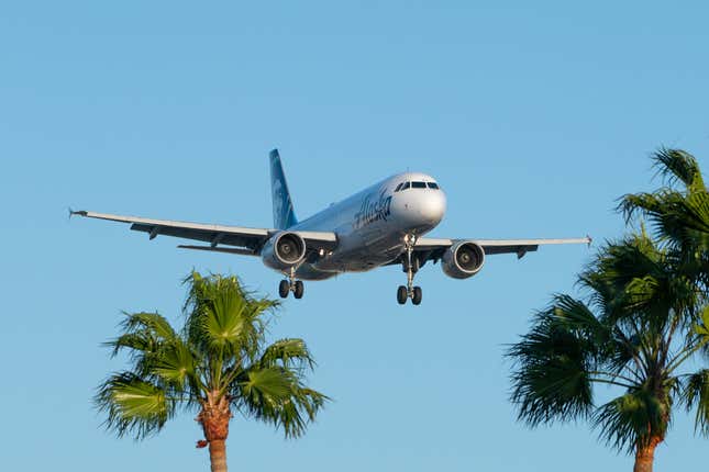 An Alaska Air flight on approach to land at LAX, with palm trees in the foreground.