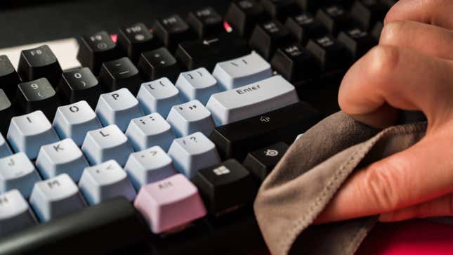 A photo of a hand moving a microfiber cloth across a mechanical keyboard 