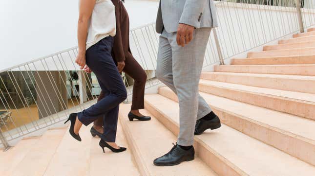 Two women in high heels walk up a set of stairs while a man in dress shoes walks down the same staircase