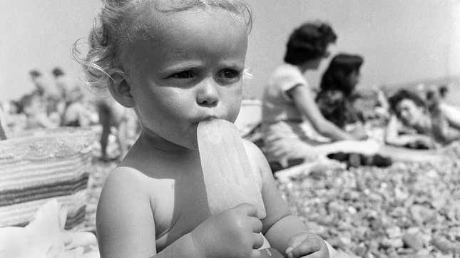 Black and white photo of baby eating popsicle on the beach
