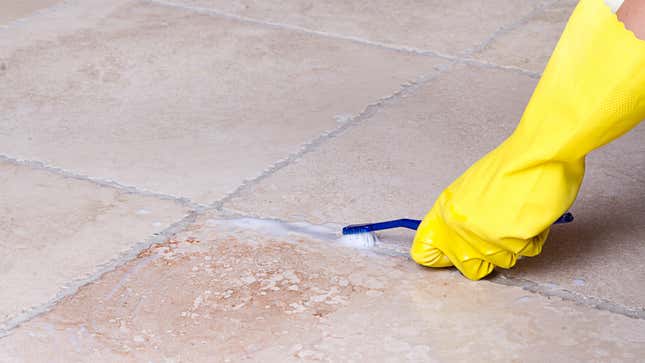 person wearing a yellow latex glove scrubbing at tile grout with a toothbrush