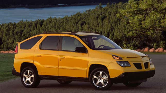 A photo of a yellow Pontiac Aztec car parked overlooking a lake. 