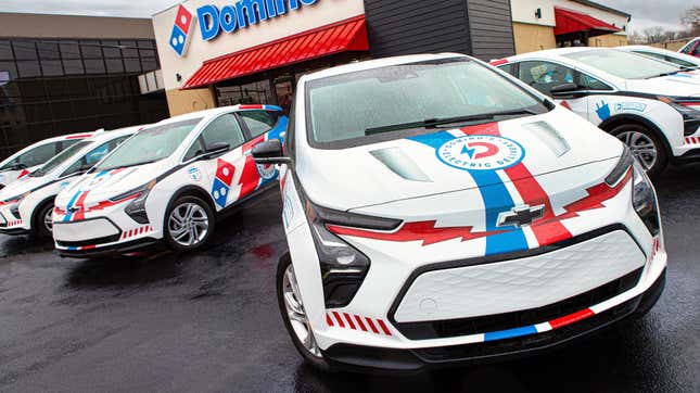 A number of Domino's liveried Chevy Bolts sitting outside of a Domino's location
