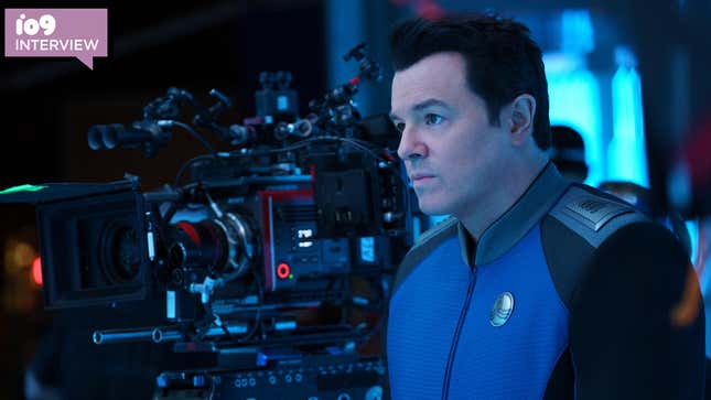 Seth MacFarlane in his Orville costume next to a camera.